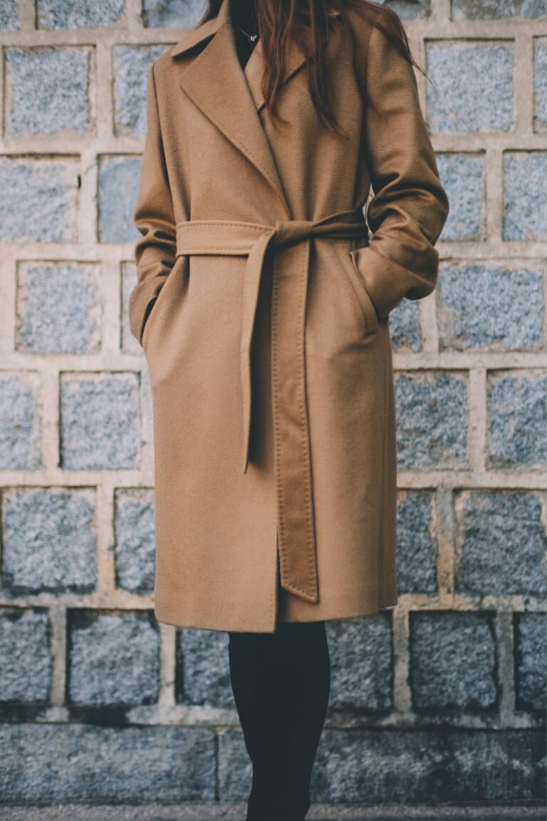 Woman in a light coat standing against a grey brick wall