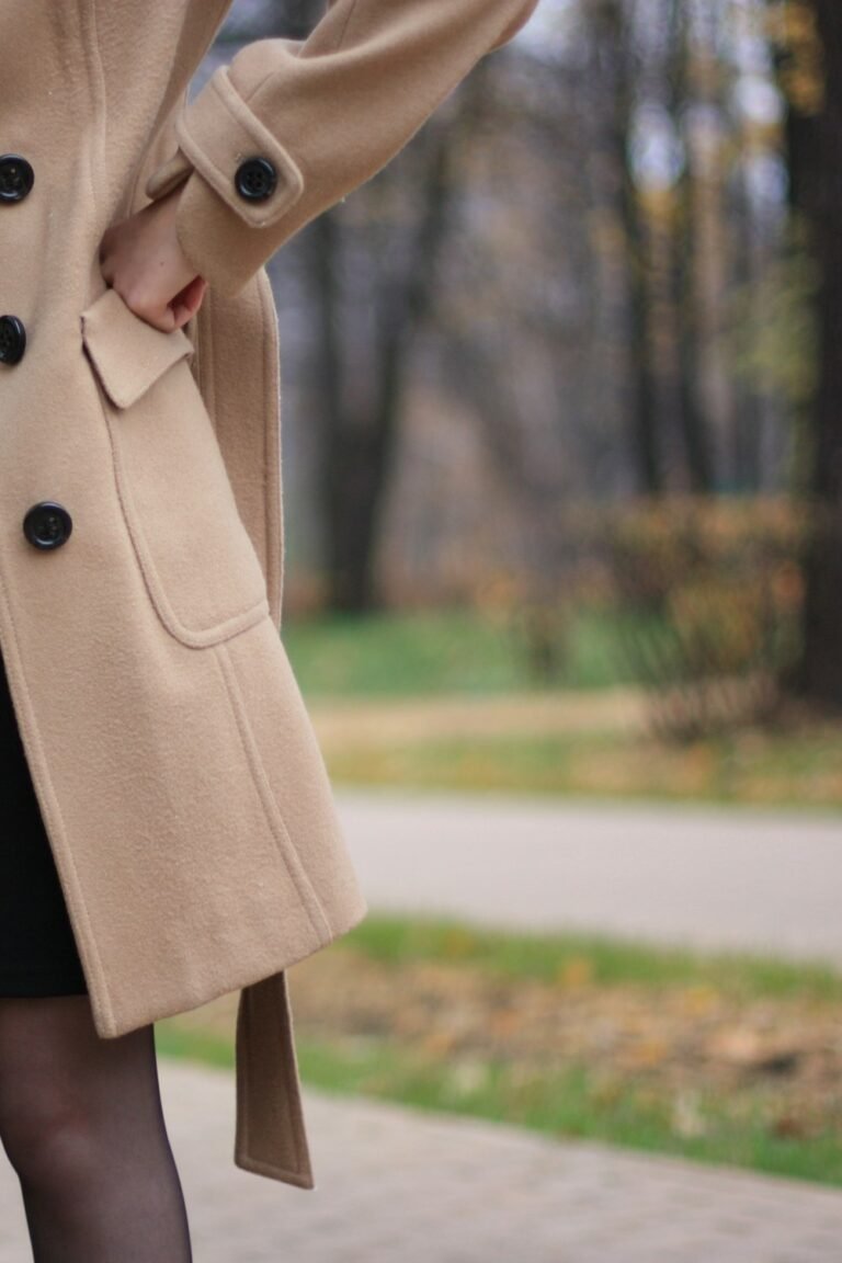 Woman in a brown coat walking outdoors in autumn light